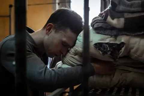 Młody mężczyzna opiera głowę na poduszce w celi. Scena z filmu o Tomaszu Komendzie, ukazująca jego trudne chwile.