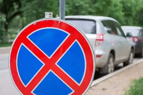 Znak zakazu zatrzymywania się b36. Samochody stoją w rzędzie przy ulicy, ale ten znak przypomina, że nie wolno tu parkować.
