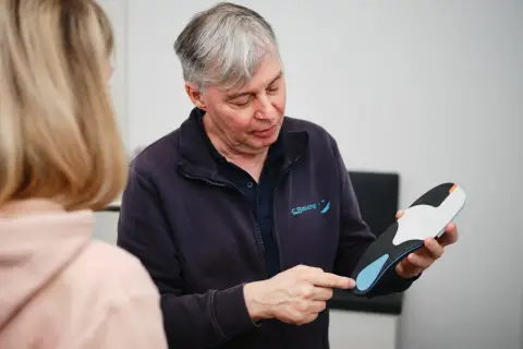 Ein Mann erklärt einer Frau, wie oft man Einlagen verschrieben bekommt, und hält eine orthopädische Einlage in der Hand.