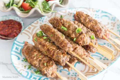 Pyszne, grillowane ćevapi na patyczkach, podane z sosem i sałatką. Idealne na letnie spotkania.