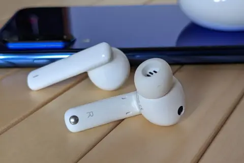 Białe słuchawki Huawei leżą obok niebieskiego smartfona. Dowiedz się, jak podłączyć bezprzewodowe słuchawki Huawei.