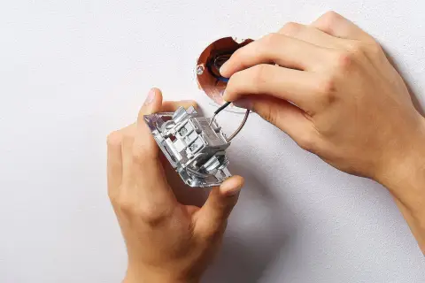 Ręce montują łącznik dwubiegunowy do ściany, podłączając przewody do mechanizmu.