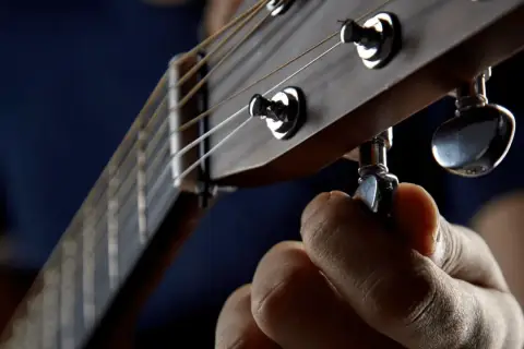 Dłoń kręci kluczem, by drop a tuning na gitarze. Idealne brzmienie jest blisko.