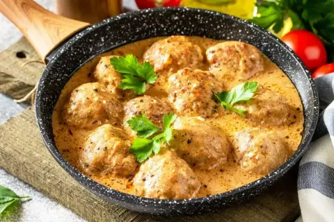 Pulpeciki w kremowym sosie, udekorowane natką pietruszki, gotowe do podania. Pyszny sos do pulpetów kusi aromatem.