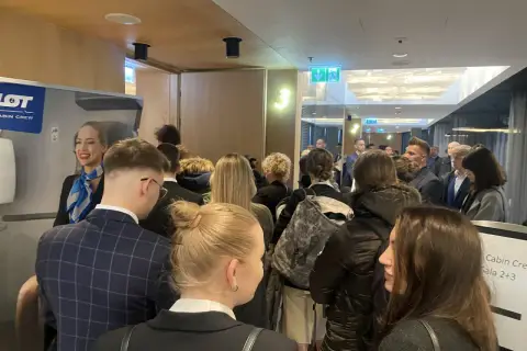 Uśmiechnięta stewardessa LOT Cabin Crew wita grupę osób. Marzenie o pracy w przestworzach zaczyna się tutaj.