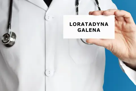Lekarz trzyma kartkę z napisem "LORATADYNA GALENA". Stetoskop wisi na jego białej katanie.