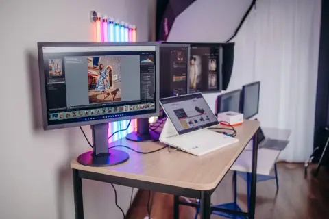 Profesjonalny monitor do obróbki zdjęć, z programem Lightroom, pokazuje zdjęcie kobiety w sukience. Obok laptop i inne monitory.
