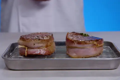 Deux filets mignons enveloppés de lard, prêts pour la cuisson, sur une grille dans un plat.
