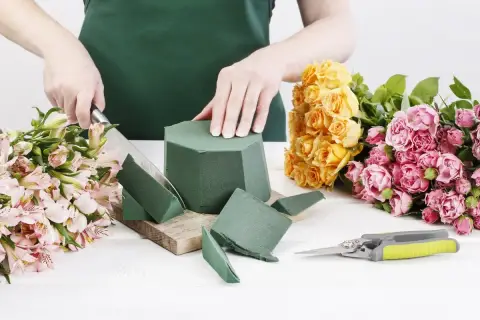 Préparation d'un bouquet : on coupe la mousse pour piquer des fleurs, entourée de roses jaunes et roses.