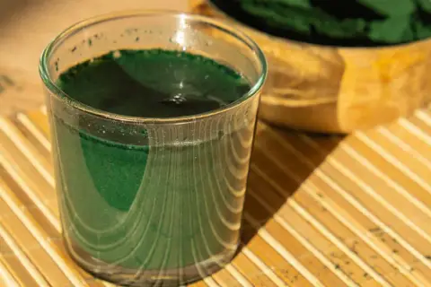 Ein Glas grüner Chlorella-Drink steht auf einem Bambusteller. Manche berichten von leichten Chlorella Nebenwirkungen wie Verdauungsbeschwerden.