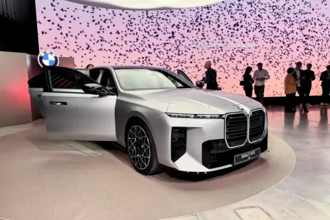 Elegancki, srebrny BMW i7 M70 G10 z otwartymi drzwiami na wystawie. Tło zdobią stylizowane ptaki i logo BMW.
