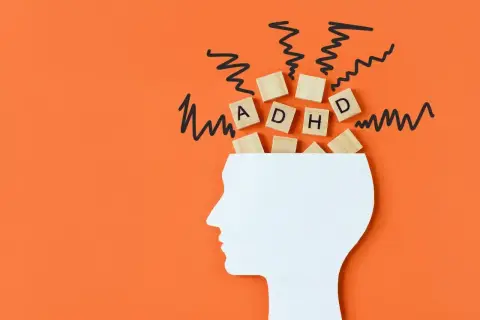 Drewniane klocki z literami "ADHD" wypadają z głowy, symbolizując chaos myśli. To wizualizacja problemów z koncentracją, które mogą pojawić się w wyniku **autyzmu nabytego**.