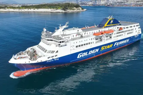 Prom "Andros King" Golden Star Ferries płynie po morzu. W tle widać port i góry.