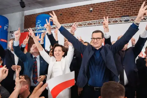 Radosny tłum z polskimi flagami i znakami zwycięstwa. W centrum Mateusz Morawiecki i inni politycy PiS, być może świętujący sukces, mimo że lista afer PiS jest długa.