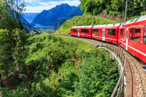 Czerwony pociąg jedzie przez malownicze szwajcarskie góry. Sprawdź swiss travel pass cena, by odkryć te widoki!
