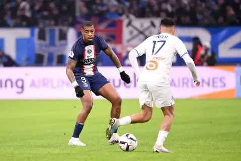 Kimpembe w ciemnym stroju PSG walczy o piłkę z zawodnikiem w białej koszulce.