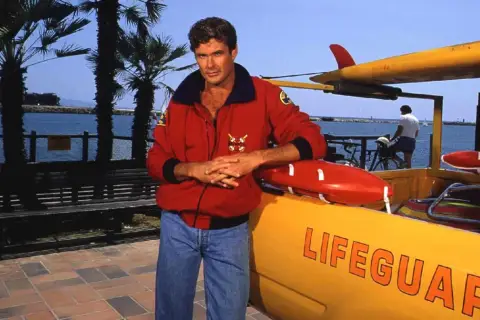 David Hasselhoff, ikona serialu Baywatch Słoneczny Patrol, pozuje przy łodzi ratowniczej.