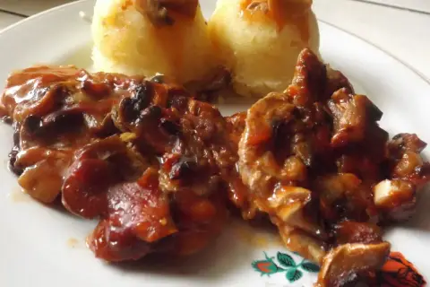 Karkówka z pieczarkami i cebulą w sosie, podana z puree ziemniaczanym. Danie polane ketchupem.