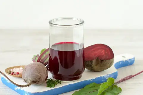 Szklanka z intensywnym, rubinowym sokiem z kiszonych buraków, obok świeże buraki i przyprawy. Zdrowie w płynie!