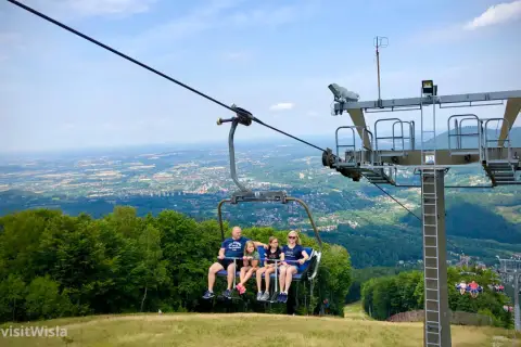 Rodzina na wyciągu krzesełkowym podziwia panoramę Wisły i okolicznych gór.