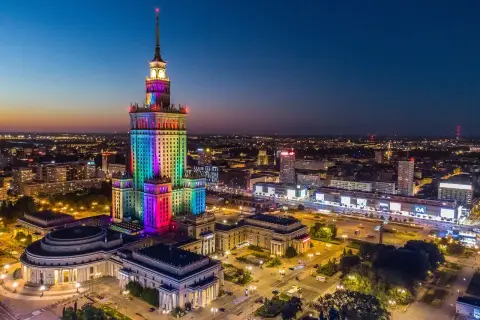 Pałac Kultury i Nauki w Warszawie, o imponującej wysokości, rozświetlony tęczowymi barwami na tle nocnego nieba.