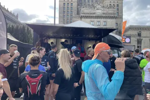 Grupa biegaczy przed budynkiem, dyskutują, czy można biegać codziennie. Na koszulkach napis "Run your way".