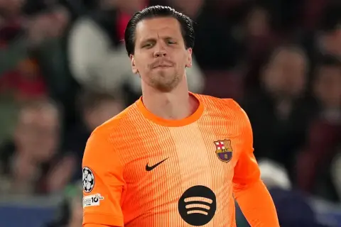 Bramkarz w pomarańczowej koszulce FC Barcelona, z herbem klubu na piersi. To właśnie w tym klubie gra Szczęsny.