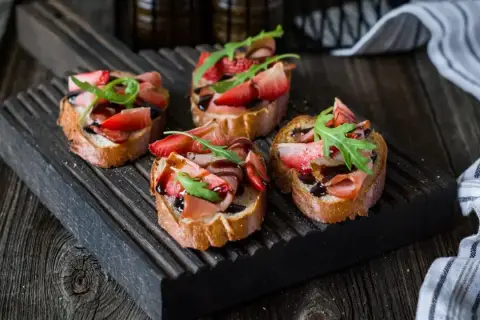 Bruschetta z truskawkami i szynką prosciutto, polana balsamicznym sosem. Idealny przepis na letnią przekąskę.