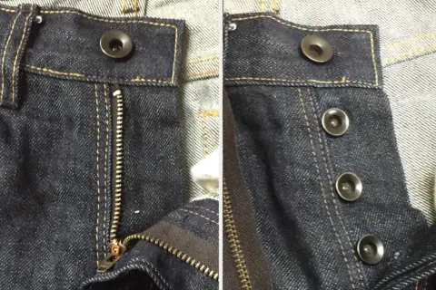 Close-up of dark wash jeans. One side shows a zipper fly with a single bouton jeans at the top. The other side displays three bouton jeans.