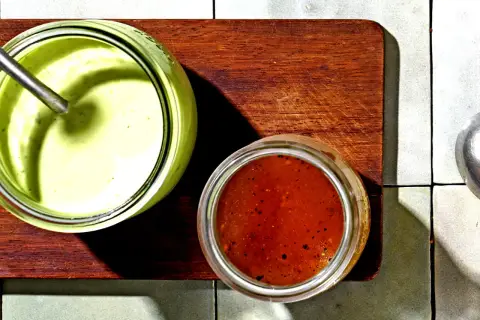 Zwei Gläser mit Saucen: ein cremiges Avocado Dressing für Salat und eine rote Vinaigrette.