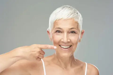 Donna sorridente indica il suo sorriso, un esempio di come rinforzare i denti a cinquant'anni con un sorriso smagliante.
