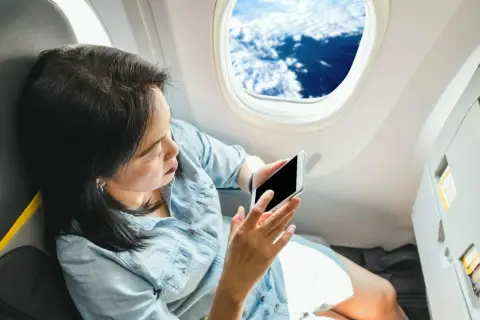 Kobieta z telefonem siedzi przy oknie w samolocie Ryanair, podziwiając widok chmur.