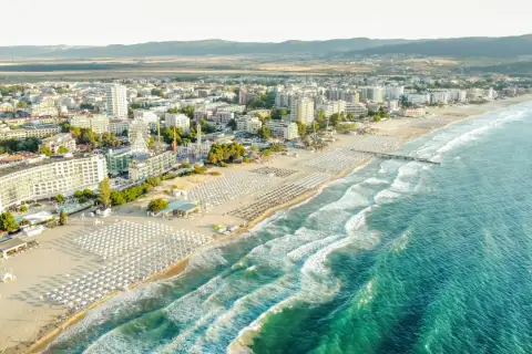Słoneczne bułgaria plaże z rzędami leżaków i parasoli, turkusowe morze i nadmorskie miasto w tle.