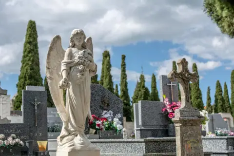 Anioł stróż na cmentarzu, symbol spokoju i pamięci. W tle wysokie cyprysy i nagrobki, tworzące melancholijną atmosferę.