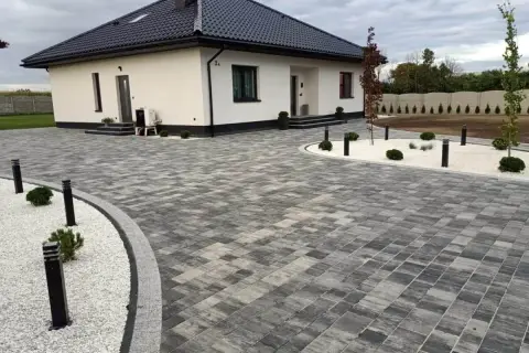 Nowoczesny dom z podjazdem z behatonu, oświetlonym stylowymi lampami.