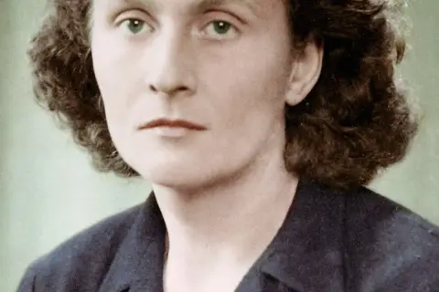 Portret Catherine Dior z zielonymi oczami i kręconymi włosami, w ciemnej marynarce.