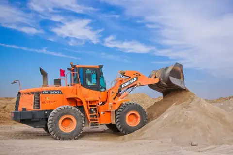 Pomarańczowa ładowarka Doosan DL300A zasypuje kopiec piasku, który może posłużyć jako żwir do betonu.