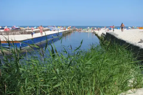 Słoneczny dzień nad kanałem w Karwi. Ludzie odpoczywają na plaży, a woda przyciąga do kąpieli. To jedna z wielu atrakcji w okolicy.