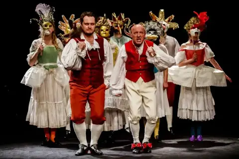 Aktorzy Teatru Ateneum w barwnych strojach i maskach, przygotowują się do wejścia na scenę.