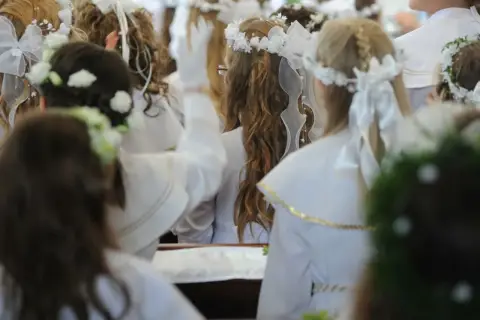 Dzieci w bieli, wianki na głowach, przygotowują się do komunii. Zastanawiasz się, ile daje chrzestny na komunię?