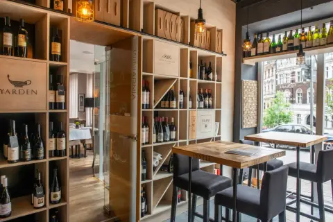 Wnętrze restauracji Muga z regałami pełnymi win, drewnianymi stołami i krzesłami barowymi.