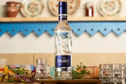 Butelka wódki Finlandia z kieliszkami i przekąskami na stole.