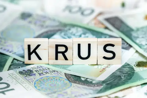 Litery KRUS na tle polskich banknotów. Zastanawiasz się, ile wynosi emerytura z KRUS?
