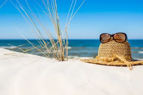 Słomkowy kapelusz z okularami przeciwsłonecznymi na piaszczystej plaży, idealny na wyjazd gdzie nad morze.