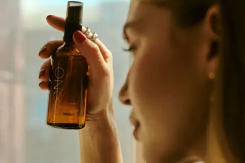 Kobieta trzyma buteleczkę z mgiełką, która zawiera alkohol cetylowy. Delikatna pielęgnacja dla skóry.