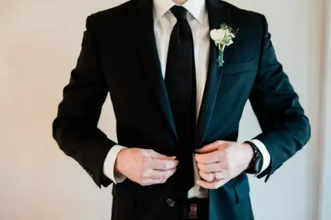 Elegancki czarny garnitur z butonierką, idealny jako jaki garnitur na wesele. Biała koszula i czarny krawat dopełniają stylizację.
