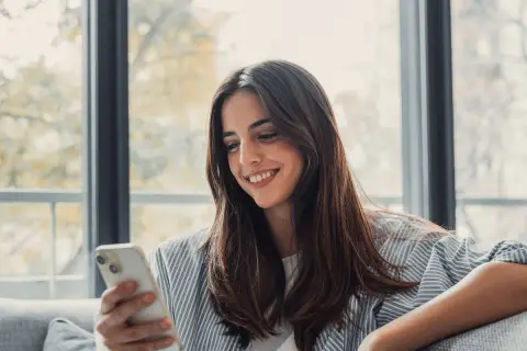 Uśmiechnięta kobieta trzyma telefon, czeka na wiadomość od ukochanej osoby. To piękny przykład, jak technologia wspiera związek na odległość.