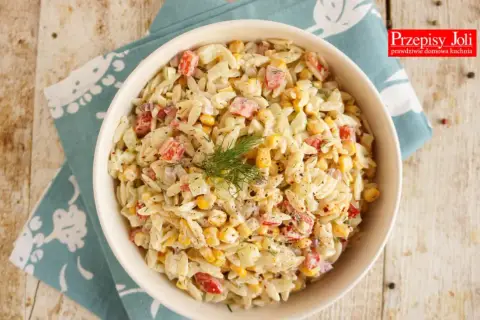 Pyszna sałatka z makaronem orzo, szynką, kukurydzą i ogórkiem, udekorowana koperkiem. Idealna na letnie dni.
