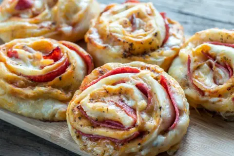 Pyszne przekąski z ciasta na pizzę z serem i wędliną, ułożone na desce.