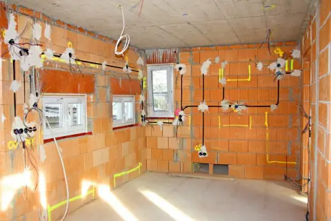 Rozprowadzona elektryka w nowym domu, widoczne przewody i puszki instalacyjne na ceglanych ścianach.